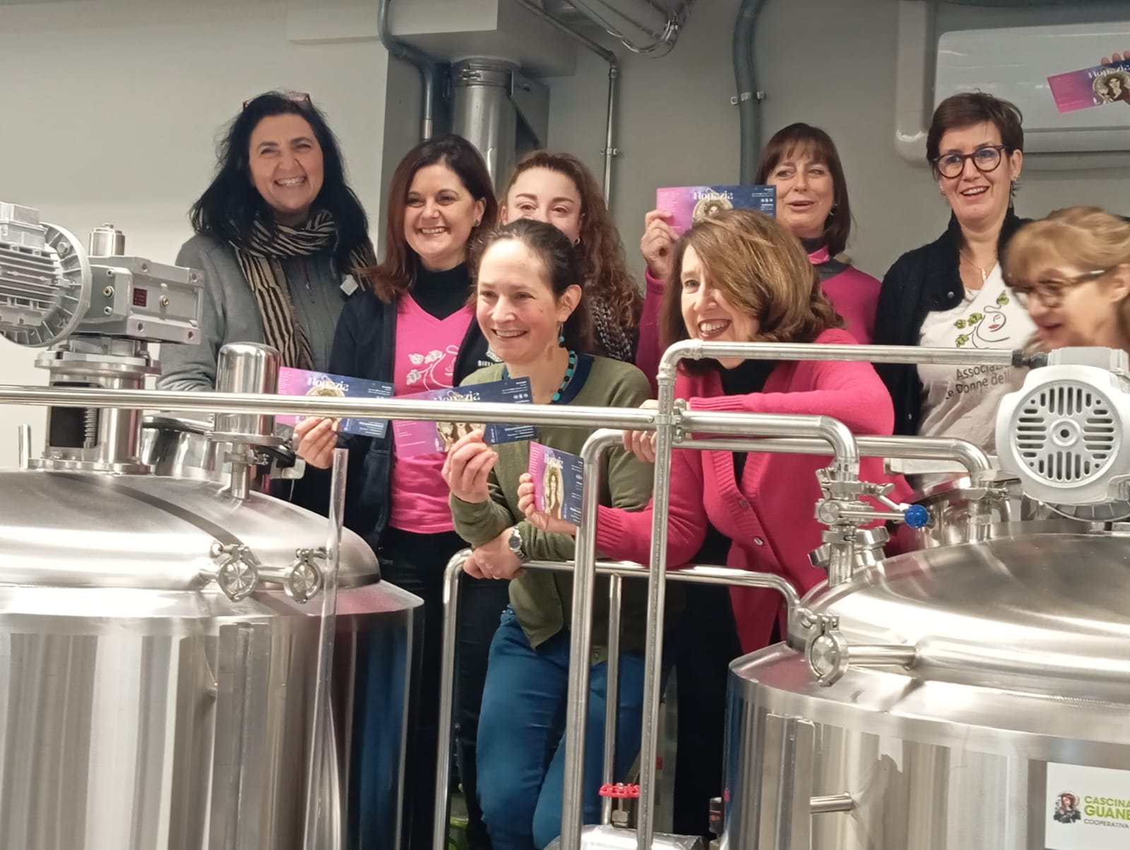 Gruppo di donne dell’Associazione Le Donne della Birra durante una cotta collaborativa nel birrificio, sorridenti accanto agli impianti di produzione.