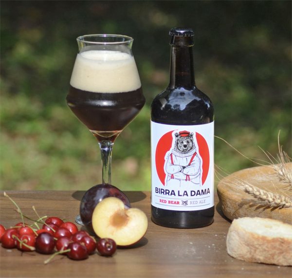 Bottiglia di birra "Birra La Dama" con bicchiere pieno, pesche fresche e ciliegie.