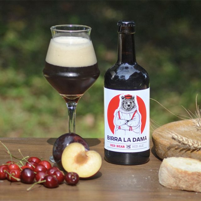 Bottiglia di birra "Birra La Dama" con bicchiere pieno, pesche fresche e ciliegie.