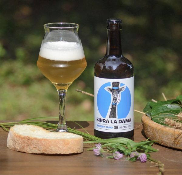 Bottiglia di birra "Birra La Dama" con bicchiere pieno, fetta di pane e fiorellini viola.