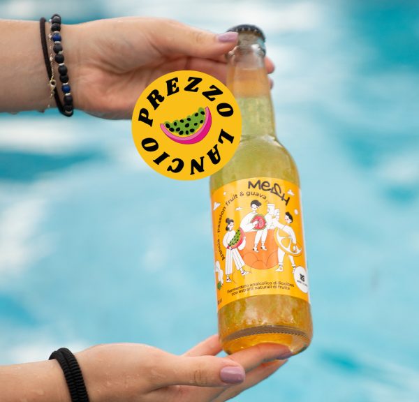 Mani che tengono una bottiglia di bevanda Mesh Orange all'arancia e frutti tropicali davanti a una piscina.